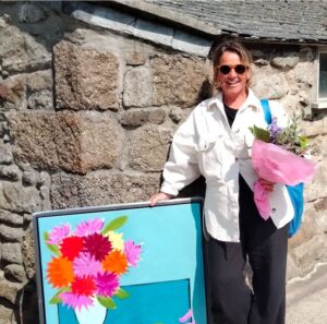 Picture of artist Iona Sanders wearing sunglasses and holding one of her colourful flower paintings
