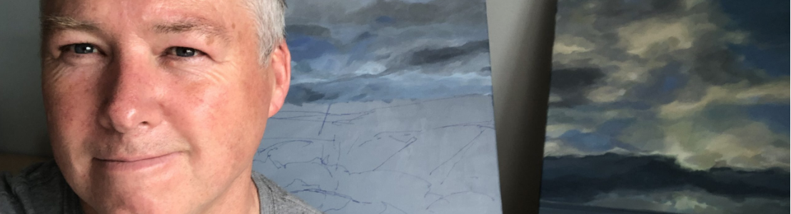 Photograph of artist nic george stood by some of his landscape paintings