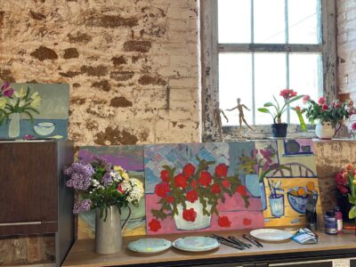 painting and vases of flowers against an old brick wall in an art studio