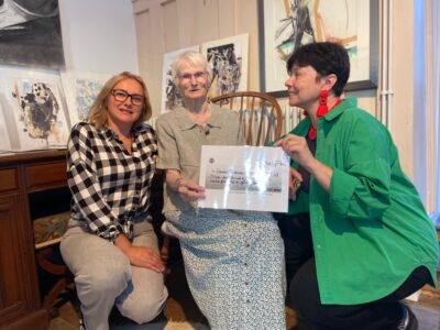 artist Anna Donovan presenting a cheque to two other woman